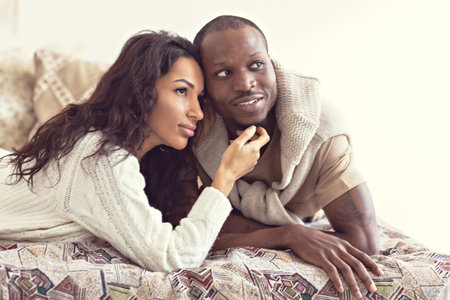 A couple in love - a black man and a mulatto woman on a bed in a bright room. Diverse family.の写真素材