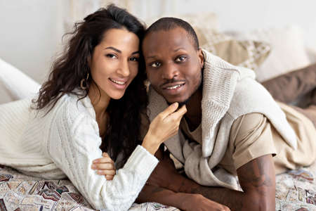 A couple in love - a black man and a mulatto woman on a bed in a bright room. Diverse family.の写真素材