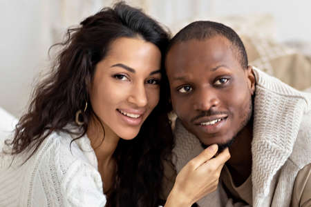 A couple in love - a black man and a mulatto woman on a bed in a bright room. Diverse family.の写真素材