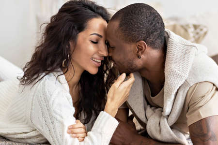 A couple in love - a black man and a mulatto woman on a bed in a bright room. Diverse family.の写真素材