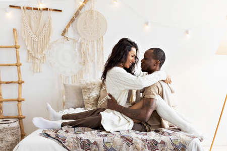 A couple in love - a black man and a mulatto woman on a bed in a bright room. Diverse family.の写真素材