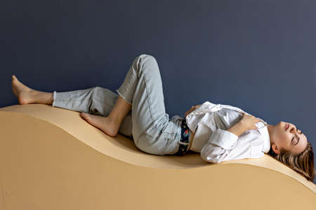 Portrait of a young woman lying on a geometric sand-colored couch.Abstract.の写真素材