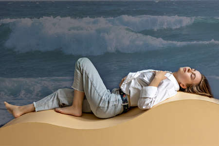 Portrait of a young woman lying on a geometric sand-colored couch.Abstract.の写真素材