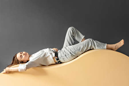 Portrait of a young woman lying on a geometric sand-colored couch.Abstract.の写真素材