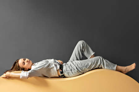 Portrait of a young woman lying on a geometric sand-colored couch.Abstract.の写真素材