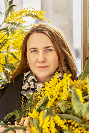Portrait of a young woman with a bouquet of mimosa in her hands. Spring.の写真素材