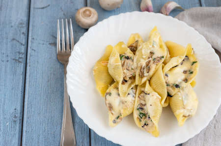 Pasta Conchiglioni with mushrooms in a white plate on wood background.の写真素材