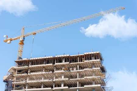 Construction crane on the background of an unfinished building and a blue sky with clouds.