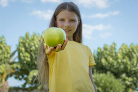 A teenage girl holds out her hand with an apple. selective focusの写真素材