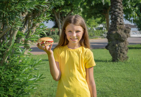 Happy teenage girl eating a burger in the park outdoors.