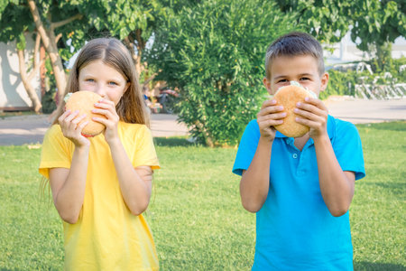 Schoolchildren eat hamburgers in the park. lunch after school.の写真素材