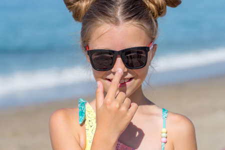 A young girl applies sunscreen to her body on the beach. Skincare while on vacation.