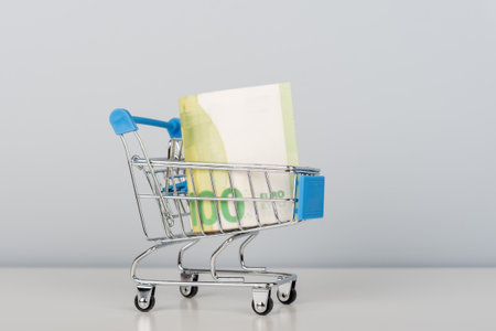 A mini grocery cart filled with banknotes on a blue background. A metaphor for earnings, investments, and abundance. The concept of financial success and growth.の写真素材