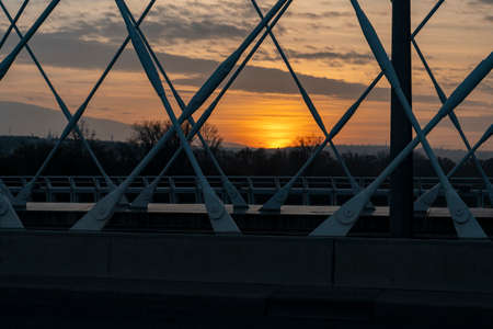 iron construction of a traffic bridge over the river in the center of the town at sunset and in the background illuminated the sky by the sun and the sunの写真素材