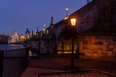 a lit lamp on the pavement under Charles Bridge at sunset and a purple sky