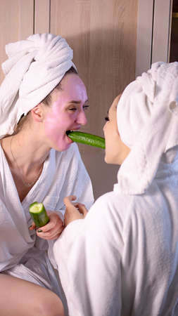 Funny young woman with facial cucumber mask. Girl with face skincare mask eat fresh cucumber on beige background .の写真素材