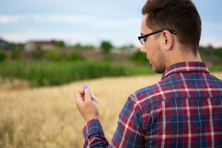 A farmer examines a plant in a wheat field. In his hand he holds a glass test tube with the test...
