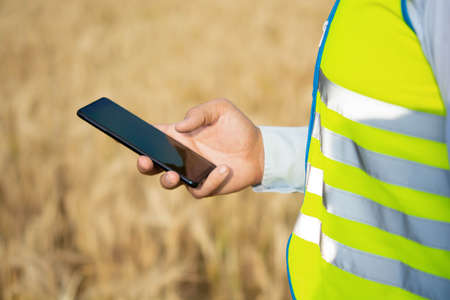 an engineer is working on his smartphone in the field, an agricultural engineer is standing in the...