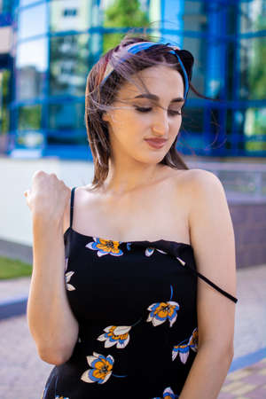 A young slender girl in a dress on a summer day against the backdrop of a tall building.