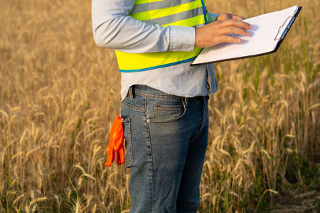 engineer in a helmet, glasses and a yellow vest, hand on a helmet, holding a notebook, a folder, making notes in a notebook a caucasian white engineerの写真素材
