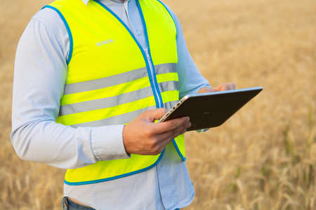 engineer in a helmet, glasses and a yellow vest, hand on a helmet, holding a notebook, a folder, making notes in a notebook a caucasian white engineerの写真素材