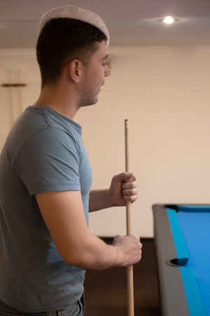 a man in a santa hat holds his hand on a pool table, plays snooker or prepares to shoot billiard...