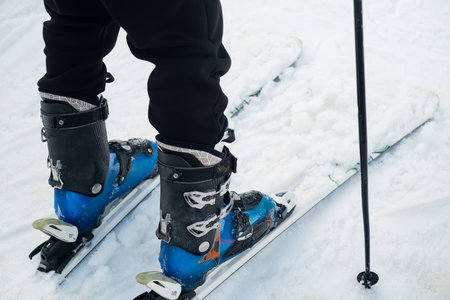 Close-up of the leg of a skier athlete in ski boots goes up on skis against the backdrop of snow-capped mountains on a sunny day. winter sports conceptの写真素材