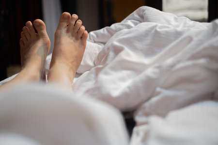Two leg of pretty girl on white bed.part of the girl's legs stick out from under the blanket, rest