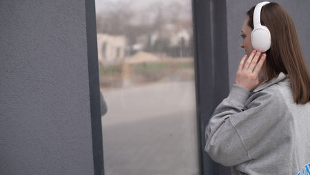 Carefree attractive brunette girl, dressed in a gray sweater, listening to music on headphones, standing on a gray backgroundの写真素材