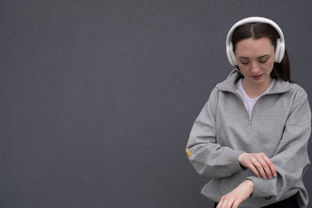 Carefree attractive brunette girl, dressed in a gray sweater, listening to music on headphones,...