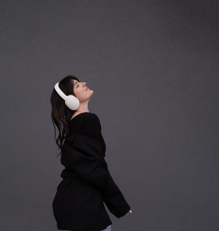 young teenager girl listens to music with headphones, dressed in a black jacket and jeans, dances to the music and sings songs loudlyの写真素材