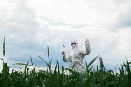 Gardener in a protective suit, mask and goggles uses a professional sprayer to treat the garden with...