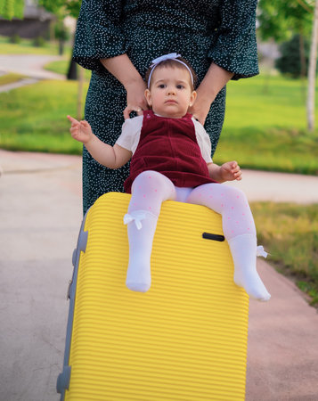 Travel concept: mom and daughter with a suitcase are preparing for a trip, a child sits on a suitcase, a mother rolls a child on a suitcase, vacation at sea, travel with familyの写真素材