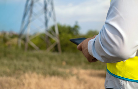A male power engineer in a white helmet checks a power line using data from electrical sensors on a...