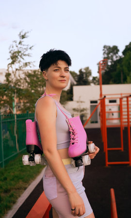 athletic woman posing with a pair of roller skates on her shoulder, smiling and looking away, sport...