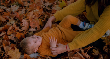 A mother and son spend quality time together, playing in the autumn park, both dressed in yellow attire. Amidst the colorful foliage, they share joyful moments, laughter echoing in the crisp air.の写真素材