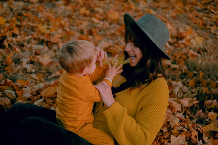 A mother and son spend quality time together, playing in the autumn park, both dressed in yellow attire. Amidst the colorful foliage, they share joyful moments, laughter echoing in the crisp air.の写真素材