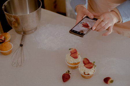 A female pastry chef takes photos on her mobile phone to advertise her business, highlighting...