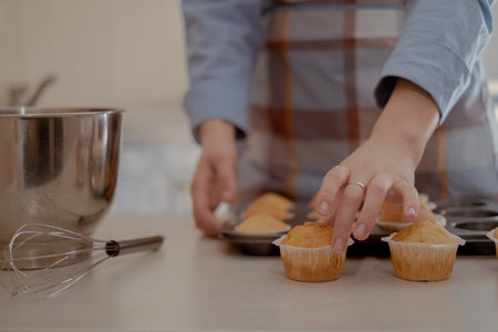 A female baker holds freshly baked cupcakes, showing her homemade pastry. Embrace the art of home...