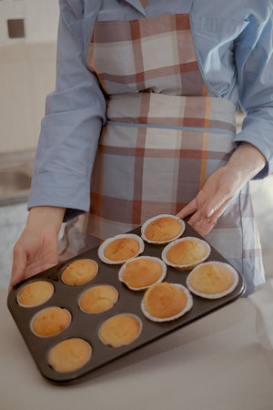 A female baker holds freshly baked cupcakes, showing her homemade pastry. Embrace the art of home...