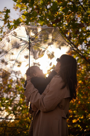 A mother and son stroll through a spring park. The woman holds a flower-adorned umbrella. It's a family walk in the park, perfect for family weekends, Parent's Day, or Mother's Day.の写真素材