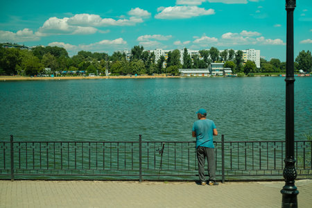 A man stands with his back, fishing in a lake in the forest, enjoying a hobby on a leisurely day outdoors.の写真素材