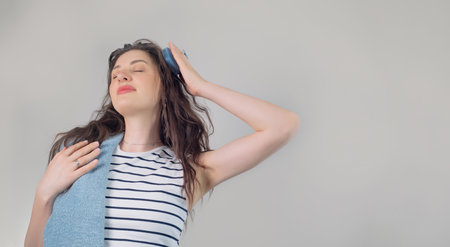 Young girl with dark curly hair using a head massager or brush to stimulate hair growth, on a white...