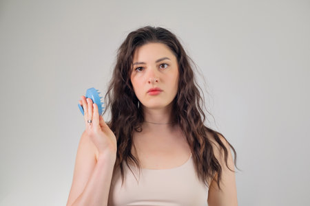 Long-haired brunette girl holding a head massager on a white background with empty space.の写真素材