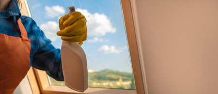 Homework for the weekend. Young pretty woman washing window in cozy living room at home. Cleaning products for home cleaningの写真素材