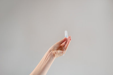 A woman's hand holds a tampon against a beige background, promoting women's health, hygiene, comfort, and sustainable, eco-friendly products.の写真素材