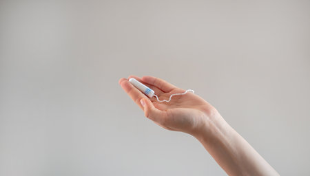 A woman's hand holds a tampon against a beige background, promoting women's health, hygiene, comfort, and sustainable, eco-friendly products.の写真素材