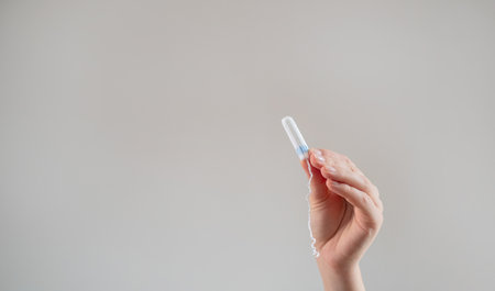 A woman's hand holds a tampon against a beige background, promoting women's health, hygiene, comfort, and sustainable, eco-friendly products.の写真素材