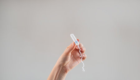 A woman's hand holds a tampon against a beige background, promoting women's health, hygiene, comfort, and sustainable, eco-friendly products.の写真素材