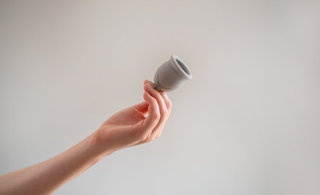 A woman's hand holds a reusable silicone menstrual cup, highlighting eco-friendly options for feminine hygiene.の写真素材